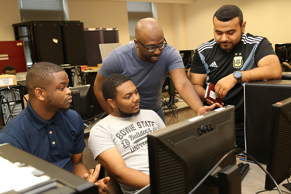 Four male students huddle around a computer screen